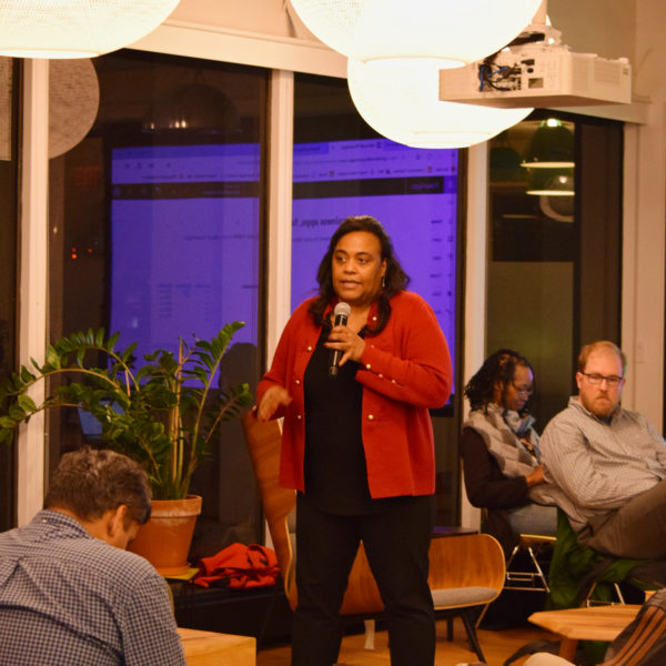 A presenter speaking to a room of people using a microphone